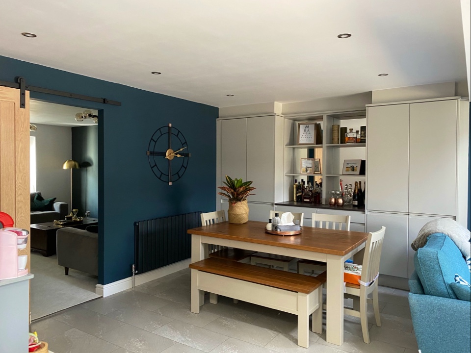 A dining space with pale fitted cabinets, open shelving and a timber table