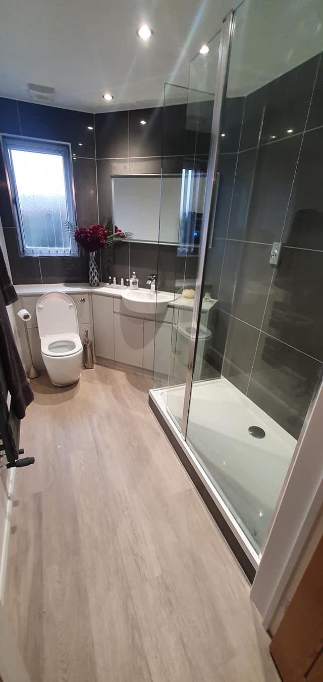 A completed bathroom with glass shower enclosure, fitted basin and grey tiling